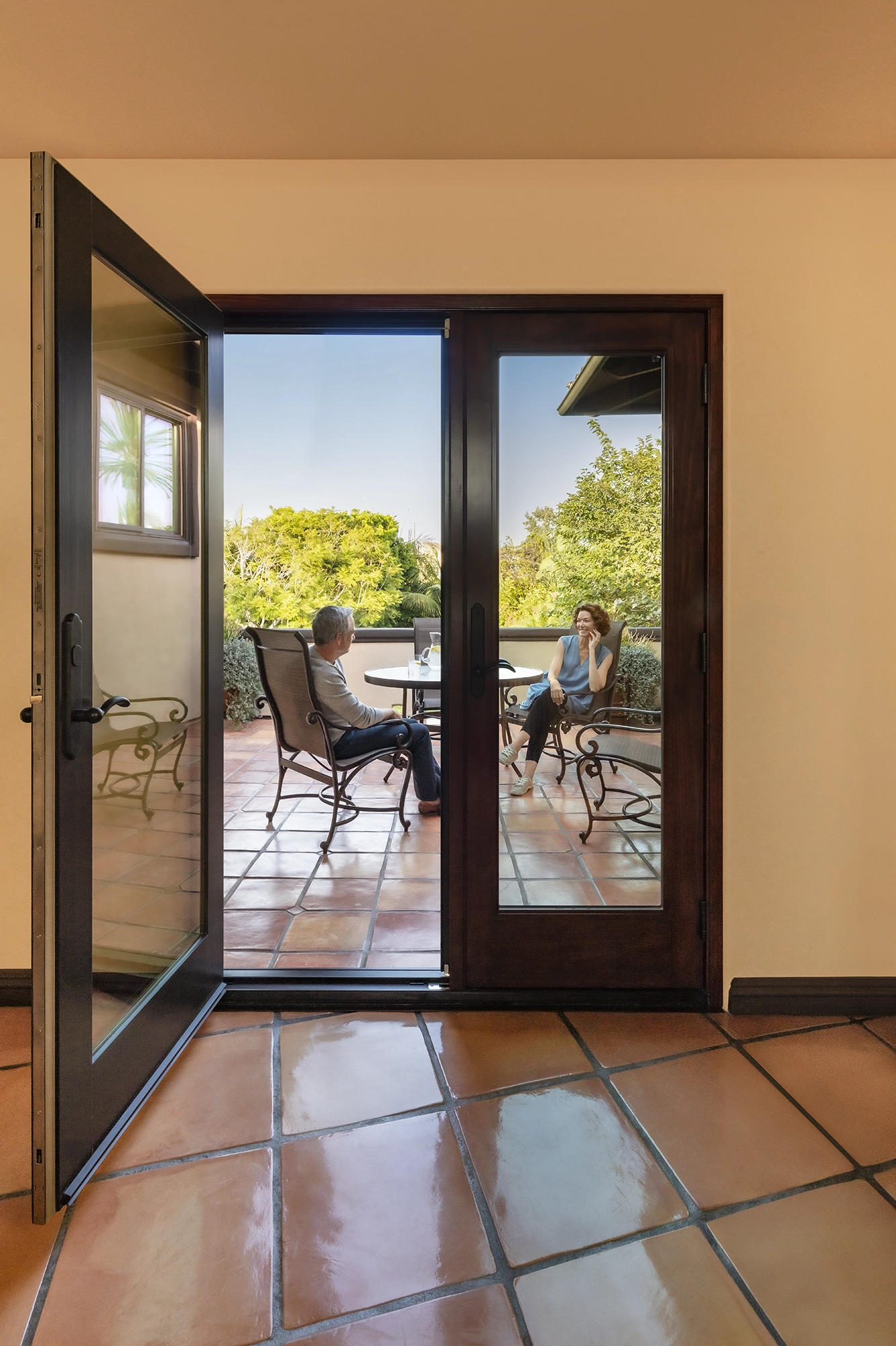 Glass doorway showing two people sitting at a patio table outdoors