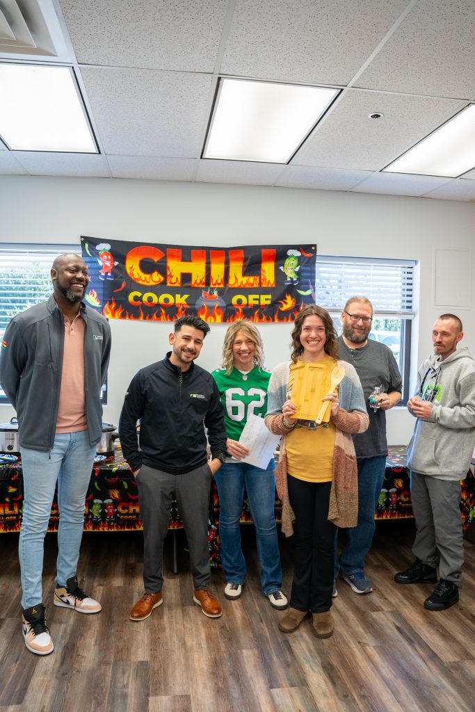 Group of people smiling with a Chili Cook Off sign behind them