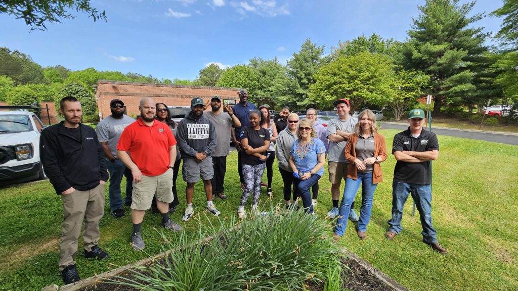 Group of people smiling outside next to a garden bed