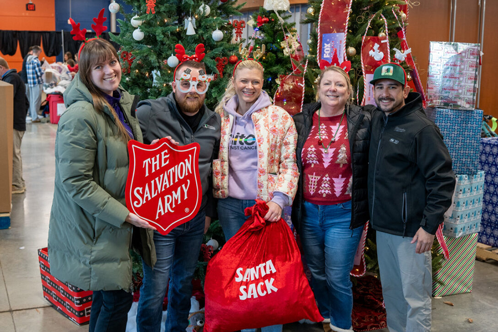 Group of people smiling in front of a Christmas tree and holding The Salvation Army badge