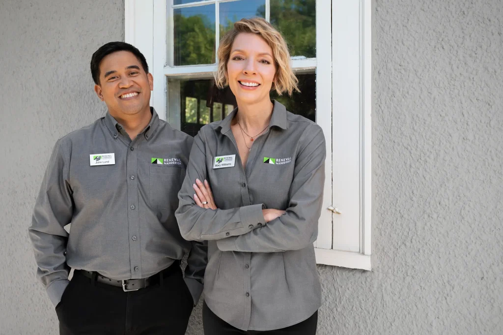 Two Renewal by Andersen employees smiling in front of a window on a gray house