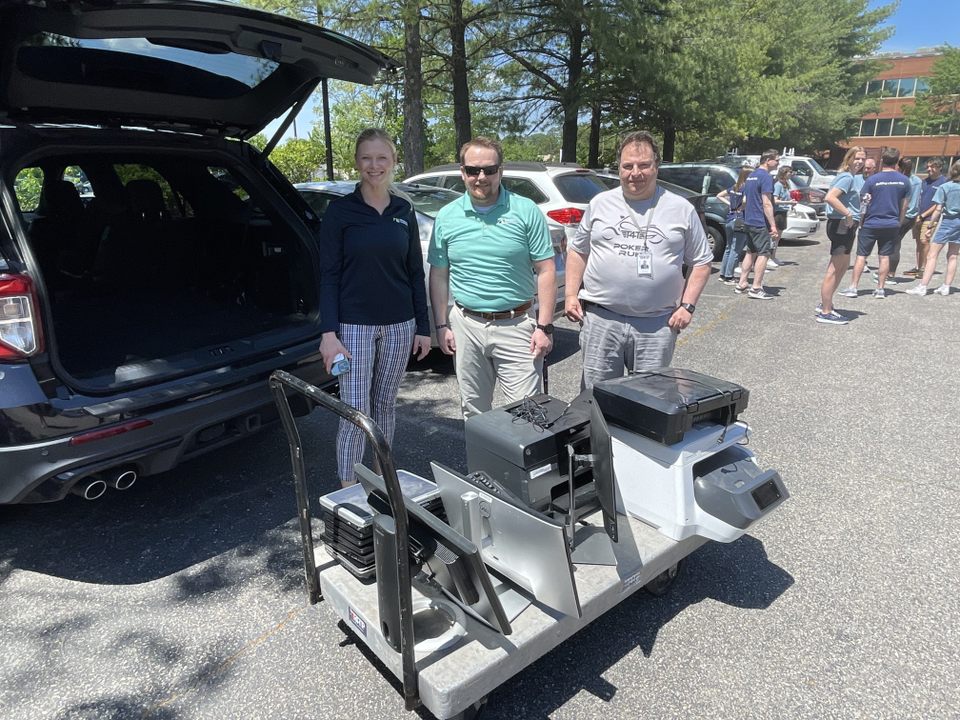 Three people smiling with a cart of office supplies