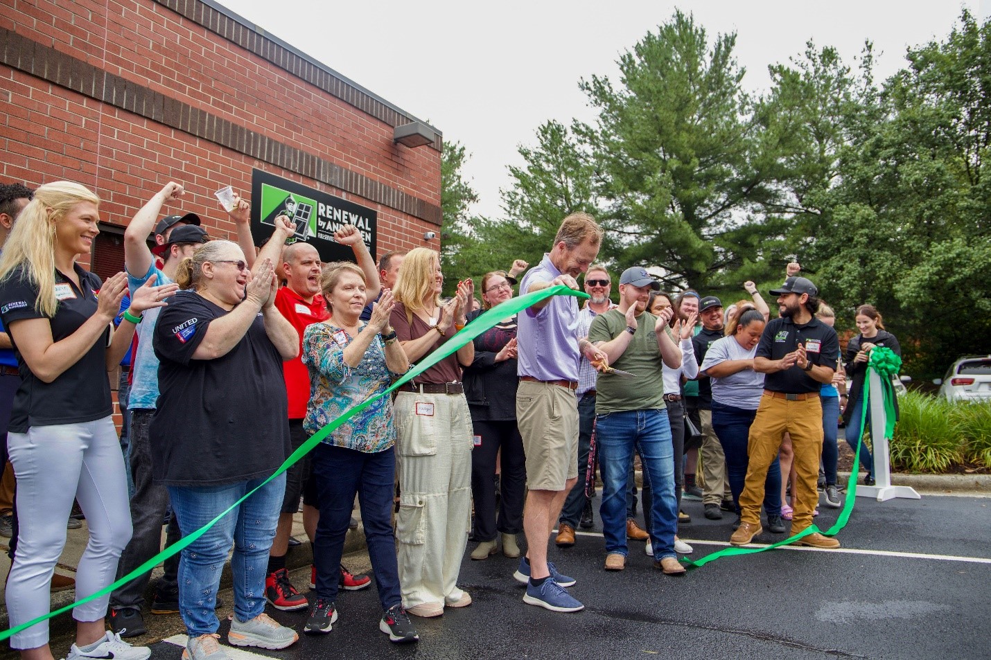 Renewal by Andersen employees celebrating while a man cuts a green ribbon outside of an office