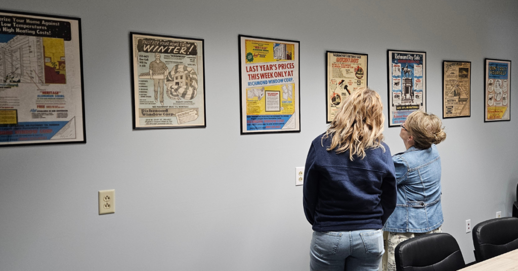 Two current employees look at vintage Richmond Window Corp posters in the conference room.